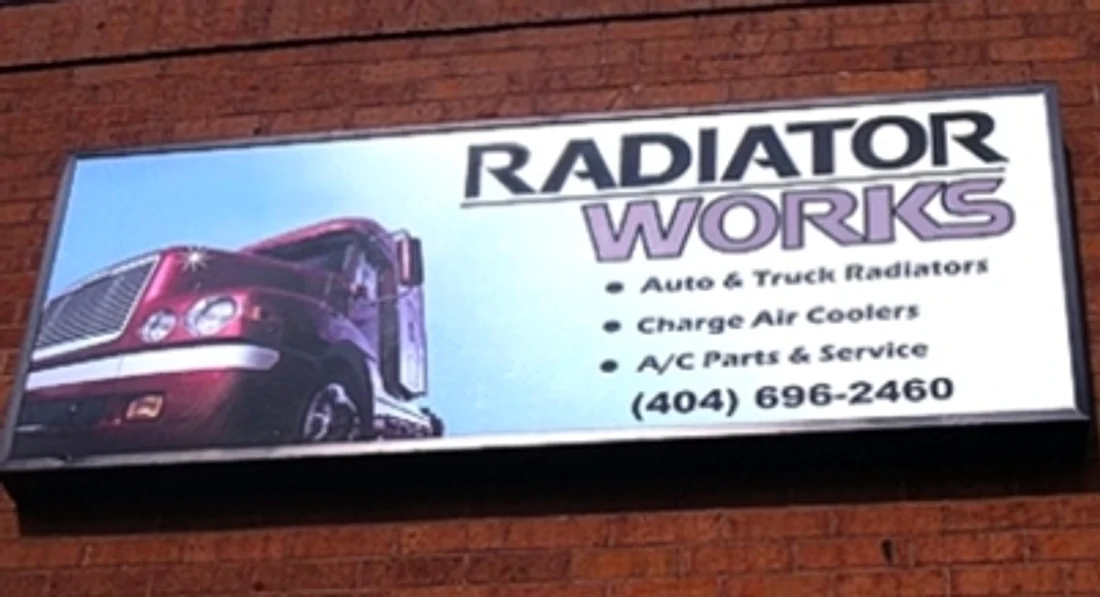 An illuminated wall sign reading “Radiator Works” with photographic truck graphics