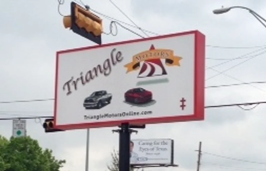 A large illuminated pole sign reading “Triangle Motors” with vehicle graphics